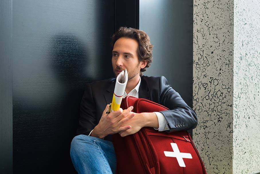 A young man with Google+ red suitcase sits waiting in front of a door