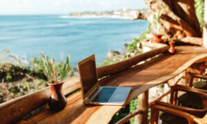 Image of a laptop on a log desk on a patio overlooking the sea